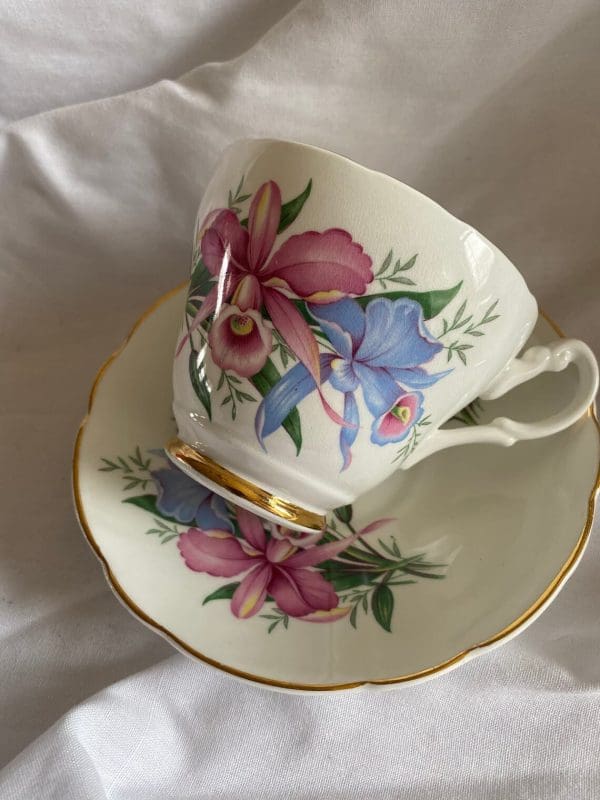 Consort tea cup with flowers design pink and blue daffodils gold trim. Tea cup is laying atop saucer