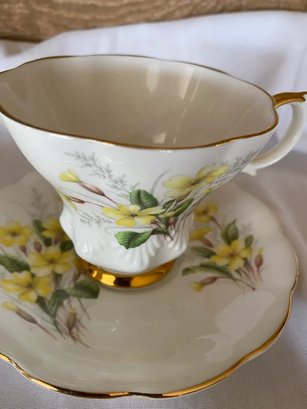 Royal Albert tea cups yellow flowers, green petals on white backdrop and gold trim close up