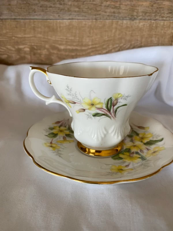 Royal Albert tea cups yellow flowers, green petals on white backdrop and gold trim side view