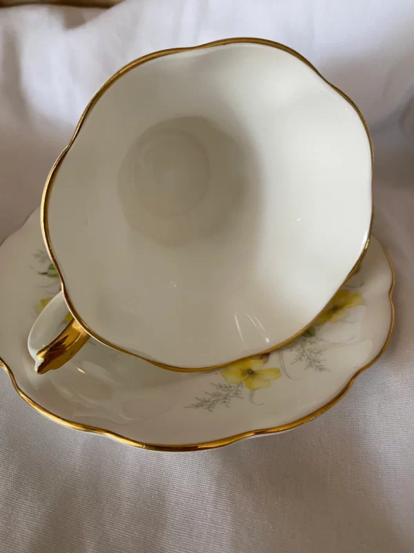 Royal Albert tea cups yellow flowers, green petals on white backdrop and gold trim white inside of cup