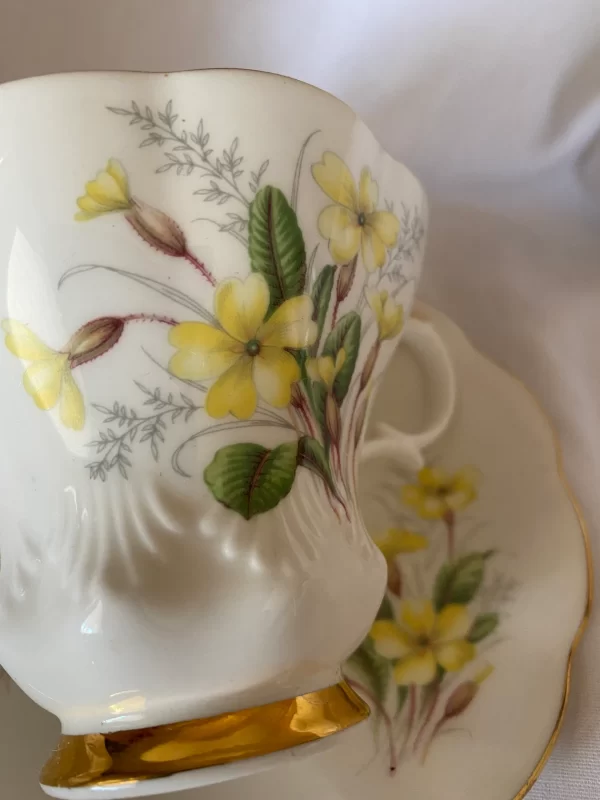 Royal Albert tea cups yellow flowers, green petals on white backdrop and gold trim close up