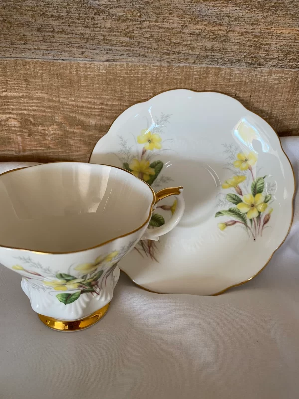 Royal Albert tea cups yellow flowers, green petals on white backdrop and gold trim zoomed out view