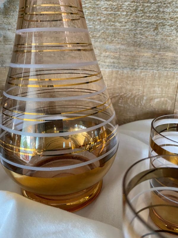 amber glass decanter with stopper gold and white stripes and four matching cups close of base of decanter